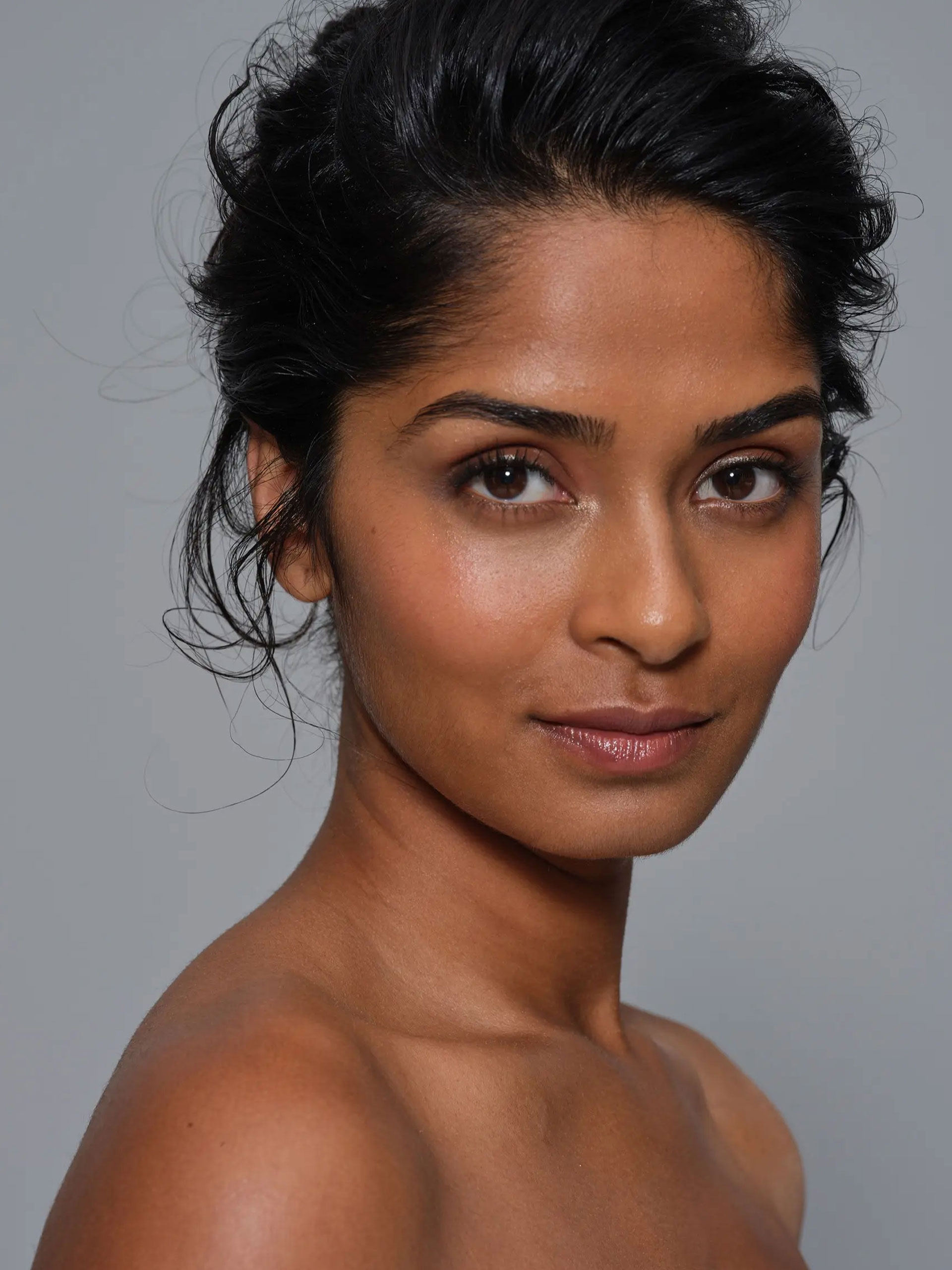 Portrait shot of an indian looking model in front of a light grey background.