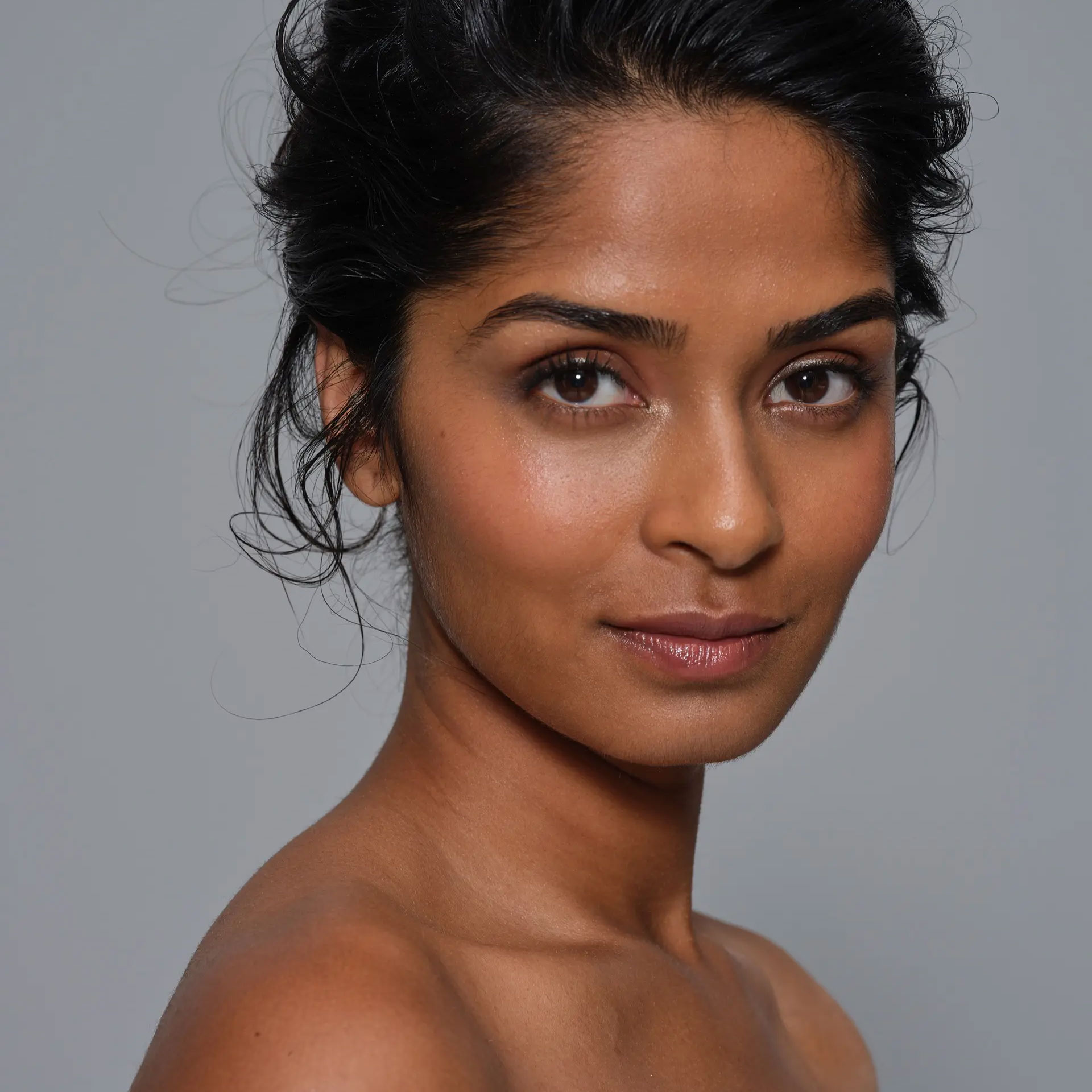 Portrait shot of an indian looking model in front of a light grey background.